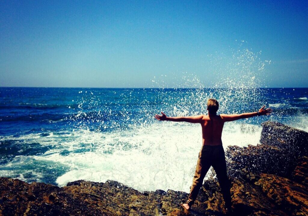 A person standing on top of a rock near the ocean.